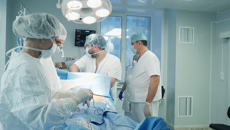 surgeons prepares equipment in clinic. female doctor adjusts cables of device over patient at coronary artery bypass surgery in clinic. medical service