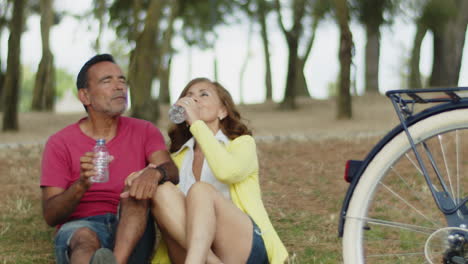 pareja sentada en el césped, disfrutando de agua potable después de andar en bicicleta