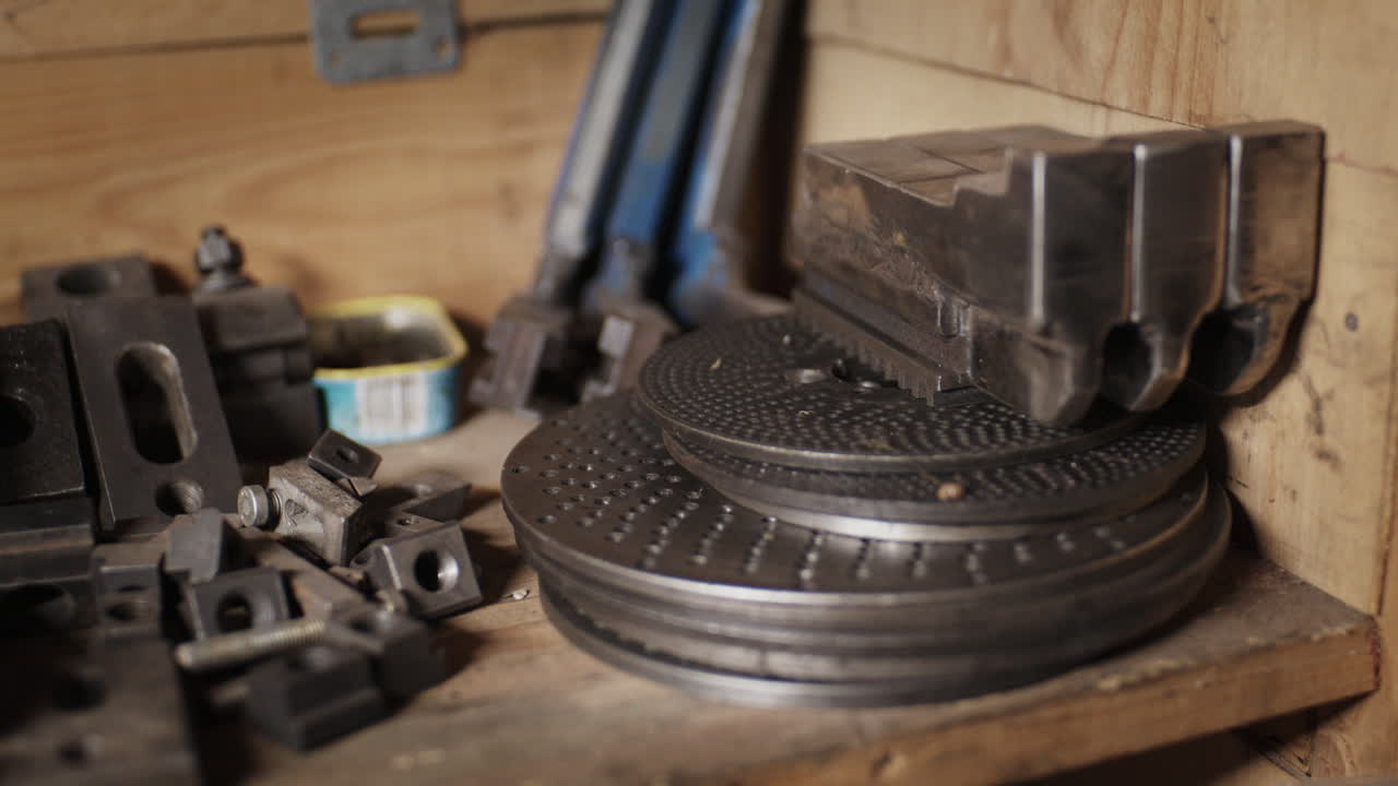 Close up of metal indexing plates, chuck jaws, and machining fixtures stored on a rustic wooden shelf in a workshop
