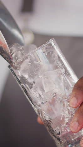 el camarero vierte piezas de hielo con una cuchara en el vidrio de primer plano. el camarero negro prepara cubos de hielo para un cóctel refrescante. bebidas frescas para los visitantes en el bar