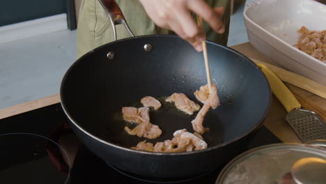 person frying meat in a wok with chopsticks