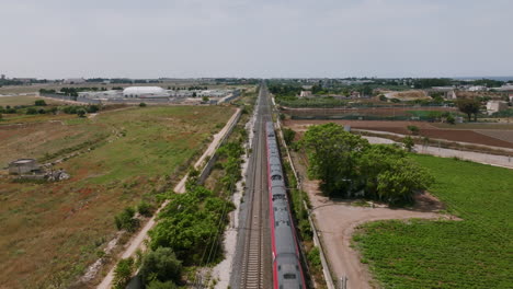 static aerial footage of a red passenger train passing underneath in bari, italy