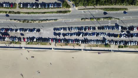 Disparo-De-Arriba-Hacia-Abajo-Del-Estacionamiento-De-La-Playa-Del-Océano-Arenoso-Con-Autos-Que-Van-Por-La-Carretera