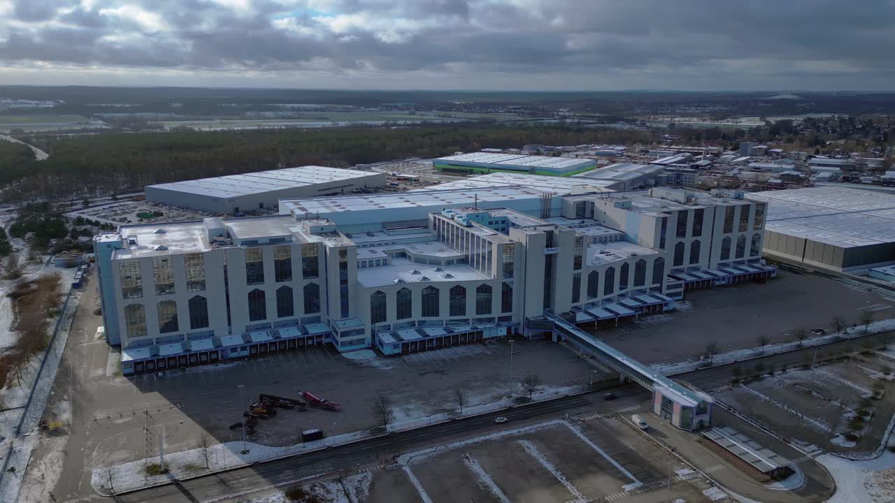 Large distribution center like an industrial castle with loading docks and parking lot under a cloudy sky in winter. Tremendous aerial view flight panorama orbit drone