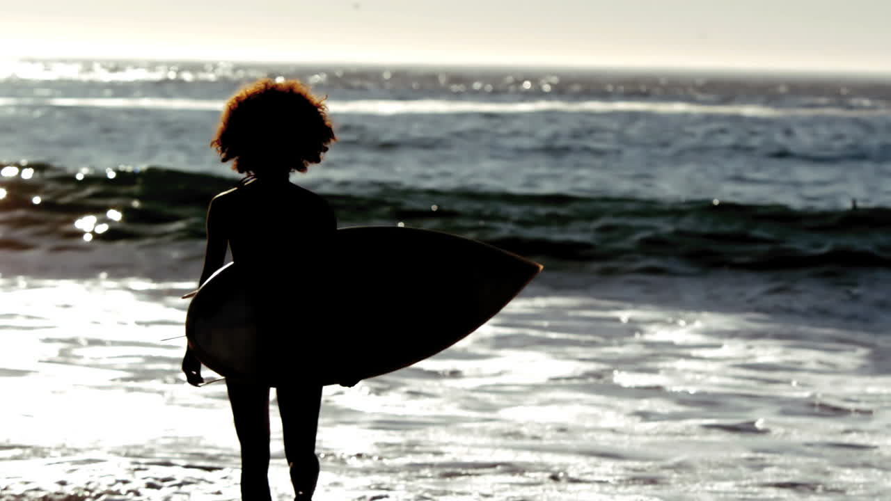silueta de una mujer corriendo por la playa con su tabla de surf
