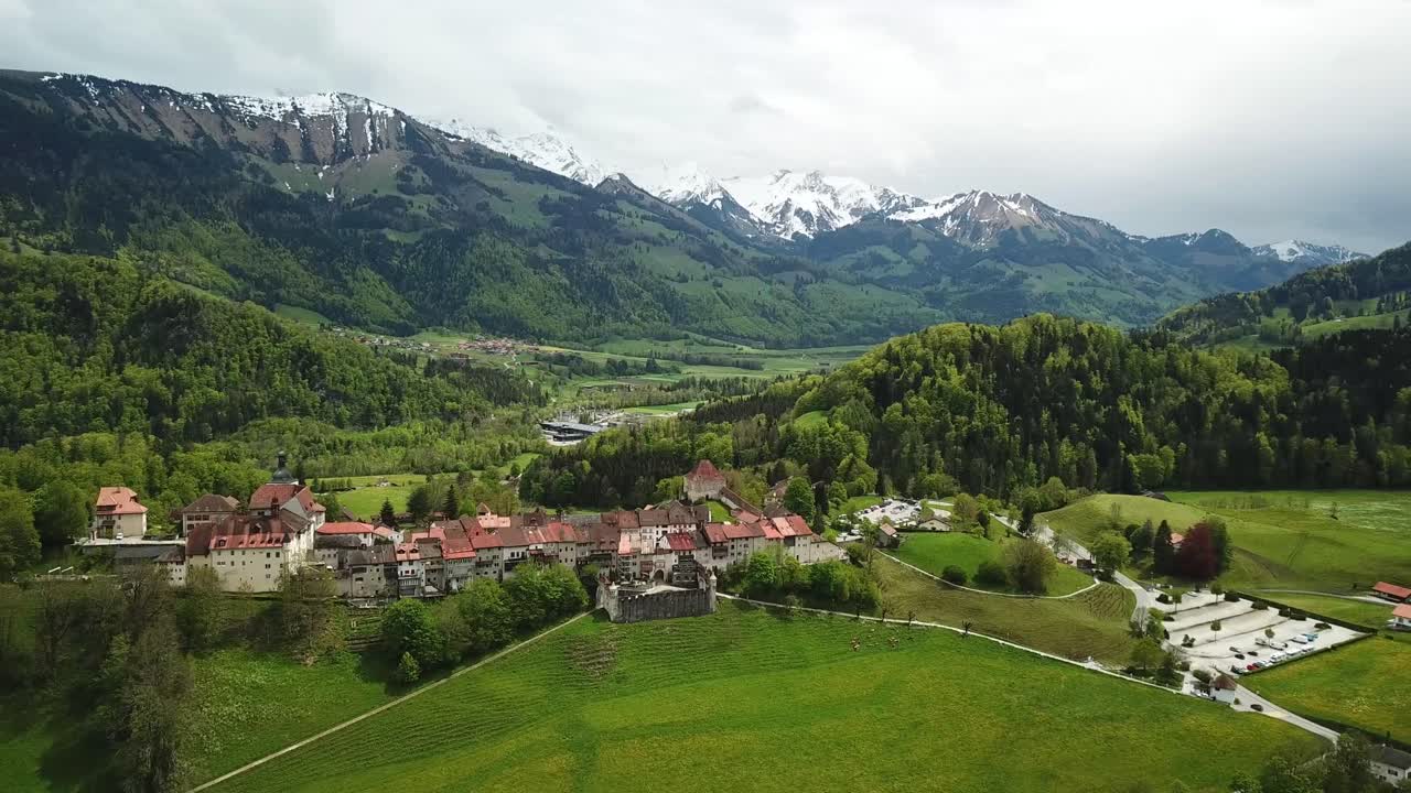 Drone shot of the idyllic town of Gruyères, in Fribourg, Switzerland with snowy Mountains as a backdrop.