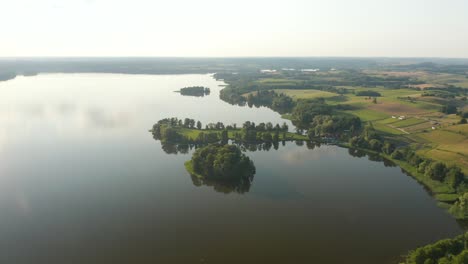 Vista-De-Un-Lago-Escénico-Con-Reflejo-De-Sol-Y-Rodeado-De-Tierras-De-Cultivo-Verdes