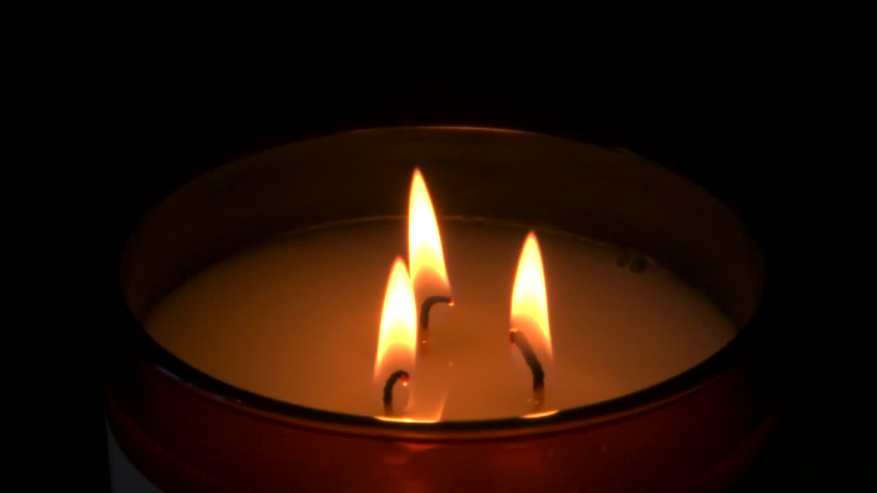 Zpomalený záběr, tři hořící svíčky s tmavým pozadím.