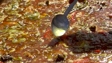 A-metal-kitchen-spoon-scoops-and-tosses-the-juices-of-a-boiling-hot-Spanish-Paella-while-it-is-being-cooked