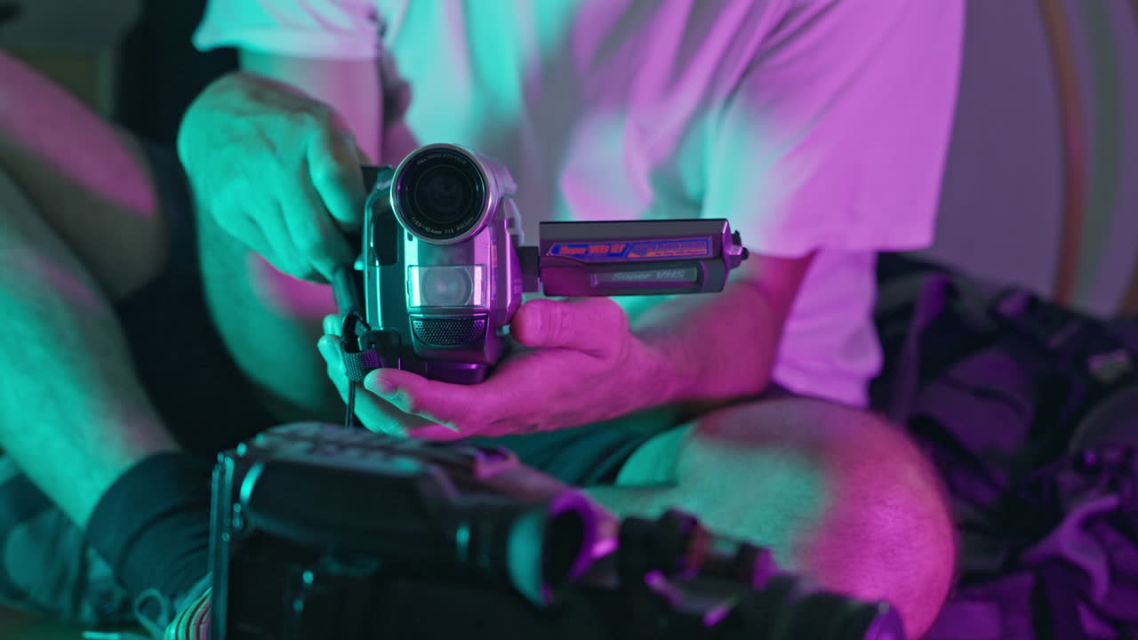 Nærbilde av hender som holder et vintage VHS-videokamera under neonlys