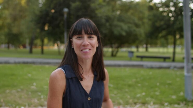 Feliz y hermosa mujer de cabello oscuro de pie en un parque de la ciudad