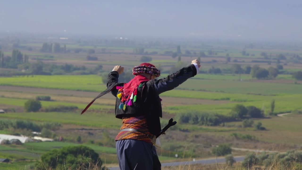 man playing zeybek with his local clothes on the hill