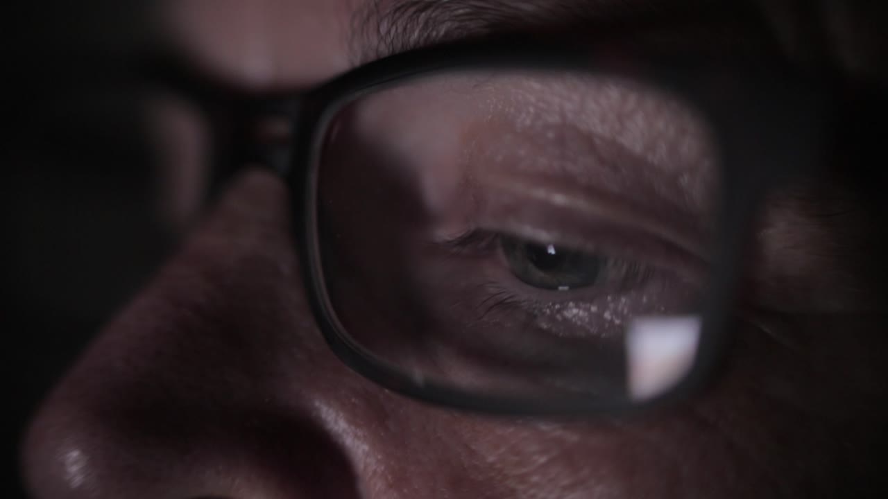 Close-up of a Person Wearing Glasses Looking at a Screen at Night
