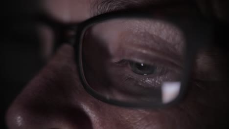 close-up of a person wearing glasses looking at a screen at night