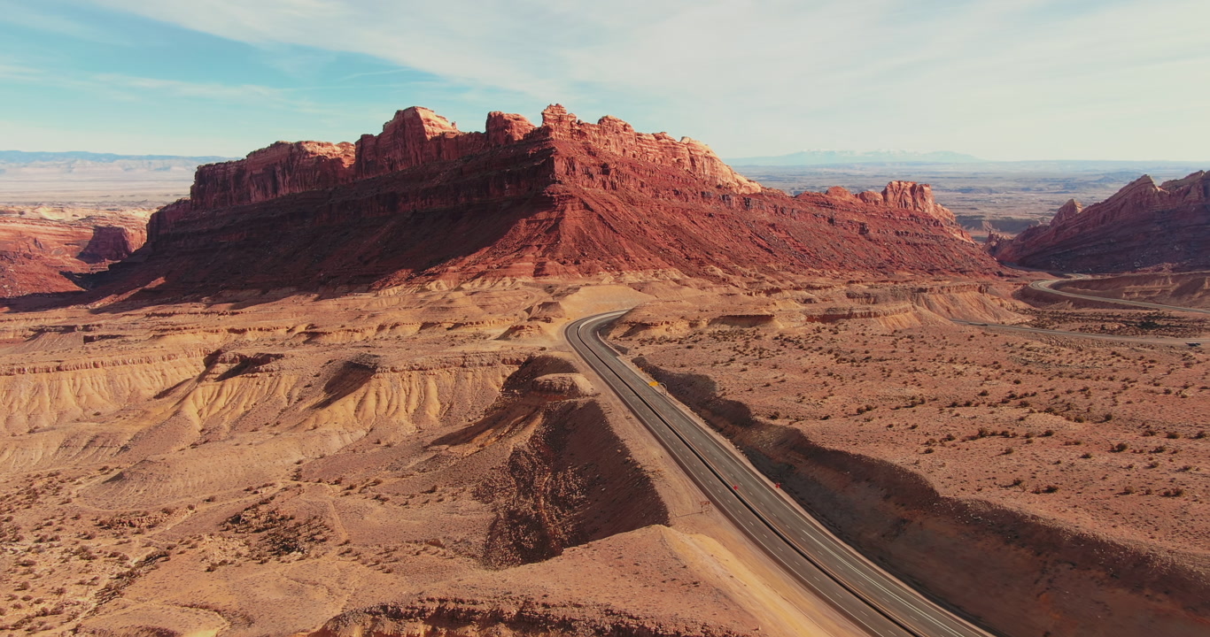 A winding highway cuts through the striking red rock formations of a desert landscape in Utah. Smooth panning camera movement
