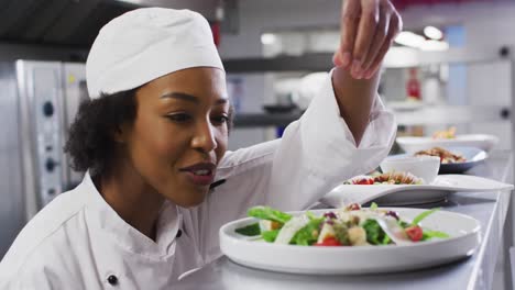 African-american-female-chef-garnishing-dish-and-similing-in-restaurant-kitchen