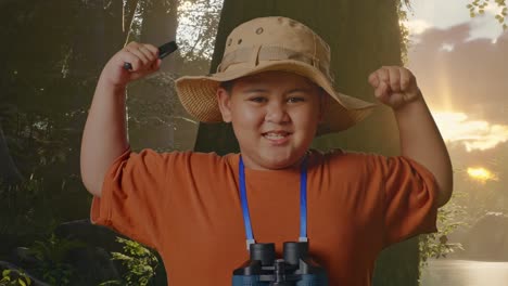 niño asiático con un sombrero y binoculares usando la lupa y luego flexionando su bíceps mientras explora la naturaleza del bosque. niño investigador examina algo, aventura de turismo de viaje, de cerca