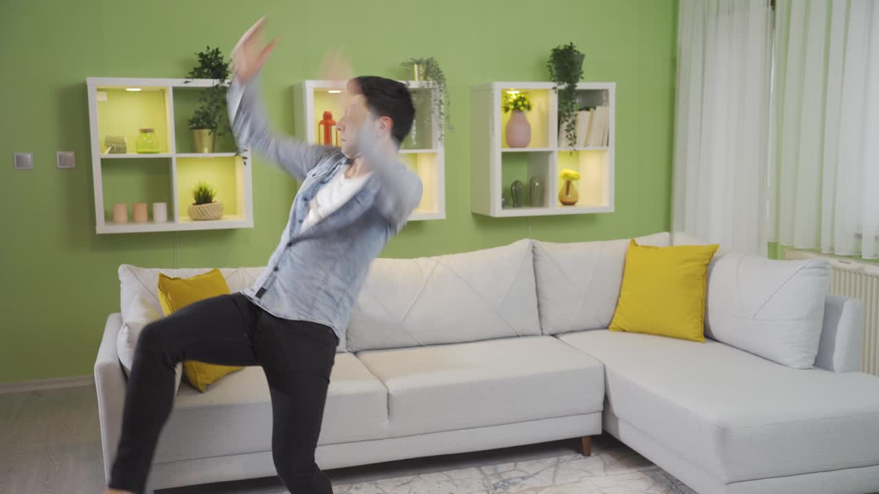 Funny clumsy young man loses balance and falls while dancing at home.