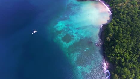 birds eye view of sailboat near coral lined islands edge with small remote beach
