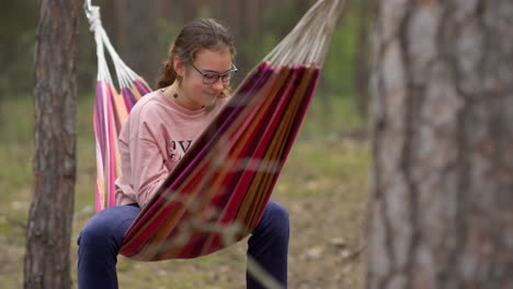 female teenager swinging in hammock with joyful mood in forest.