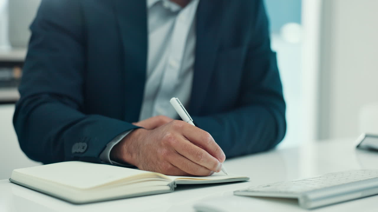 Businessman Writing Notes in a Notebook at Office Desk