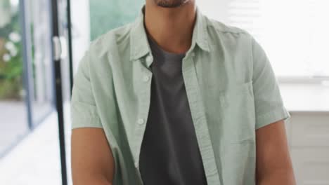 Happy-biracial-man-sitting-at-table-in-kitchen-reading-braille