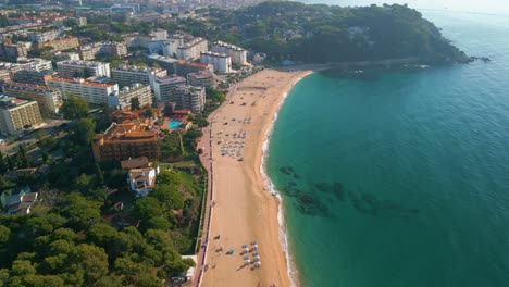 Vistas-Aéreas-De-La-Playa-Del-Mar-Mediterráneo-En-Lloret-De-Mar,-Hoteles-De-Cinco-Estrellas-En-Primera-Línea,-Vegetación,-Mar-Transparente,-Rocas-Al-Fondo