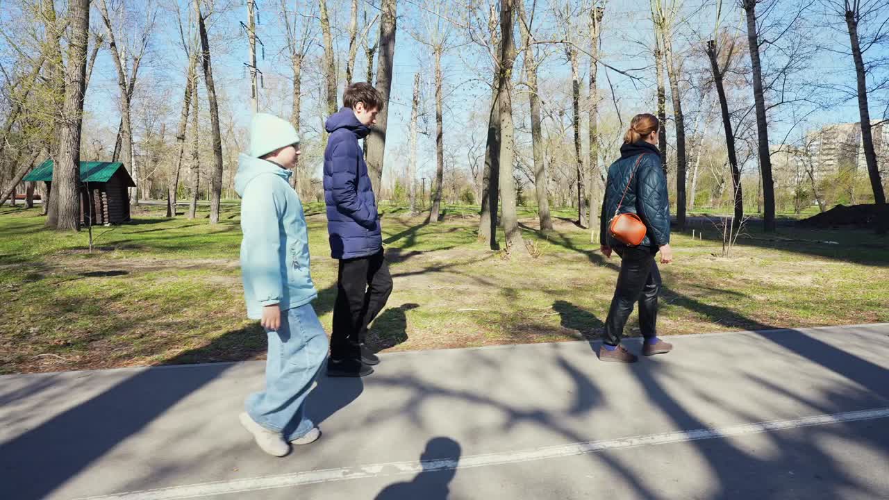 Drie mensen lopen op een verhard pad in een zonnig park.