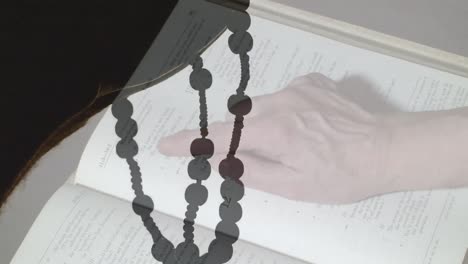 animation of caucasian woman reading bible over hands with rosary