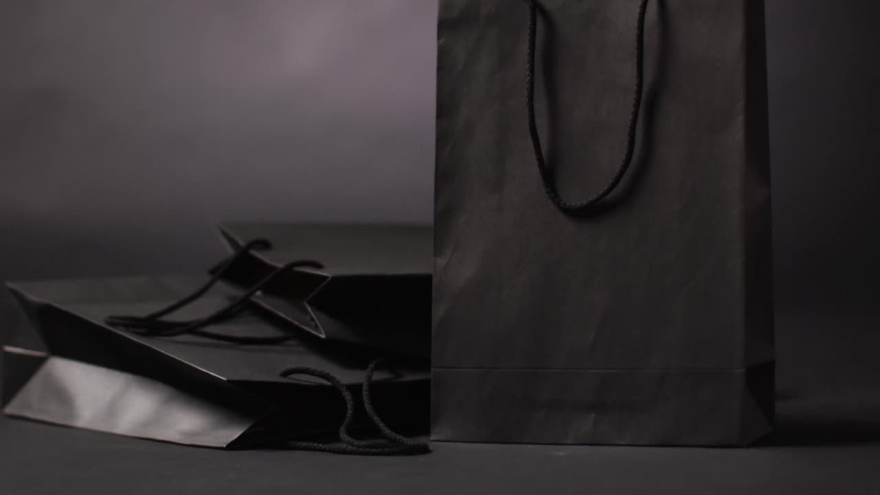Sacolas de presente pretas com alças pretas em fundo cinza escuro com espaço para texto