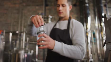 caucasian man working at gin distillery, wearing apron, fastening lid on bottle of gin