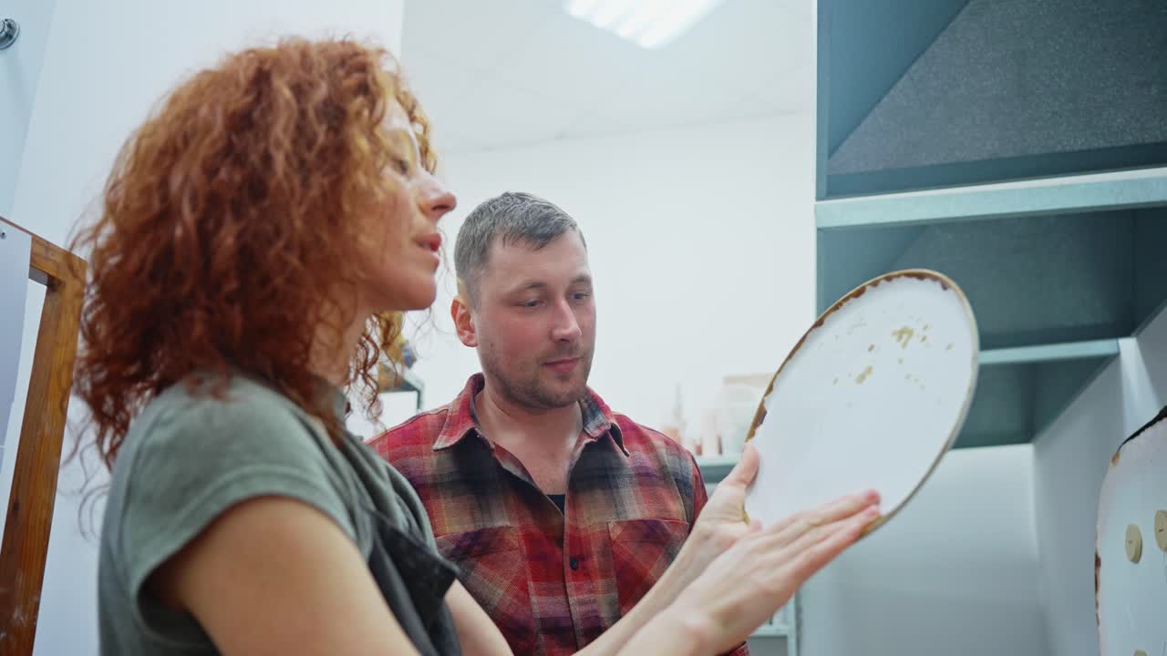 Couple Inspecting Ceramic Plates in a Workshop