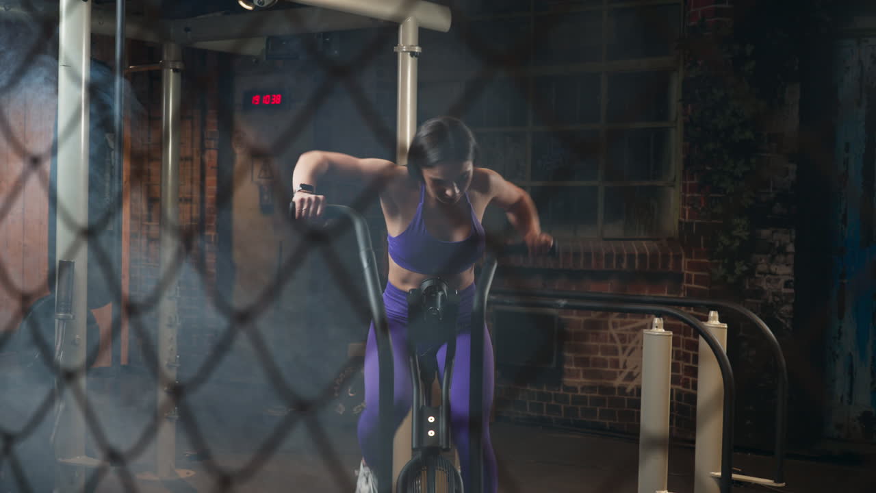 Fit woman doing elliptical trainer in a smoky indoor gym room