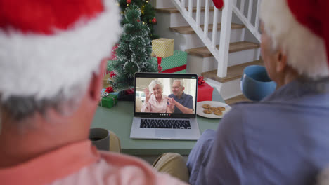 Feliz-Pareja-De-Ancianos-Caucásicos-En-Una-Videollamada-Portátil-Con-Una-Pareja-De-Ancianos-En-Navidad