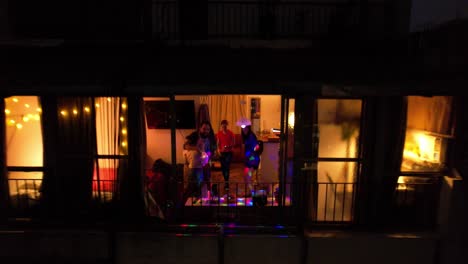 group of friends partying in an apartment, shot from outside dolly out, colored lights