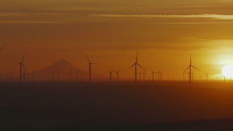 wind turbines backlit with bright and golden sunset at wind farm in oregon, usa. - wide panning