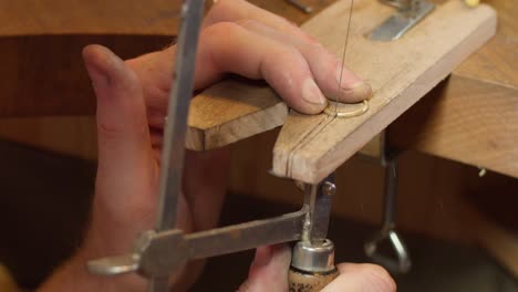 jeweller sawing in a gold ring in his workshop while making a wedding ring handcrafted