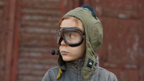 retrato de un lindo niño pelirrojo con sombrero de aviador y gafas girando la cara y sonriendo a la cámara