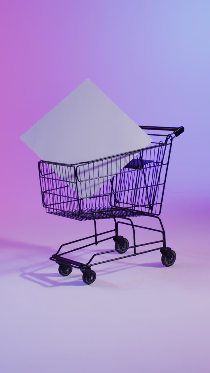 Vertical video of shopping trolley with white canvas with copy space over pink neon background