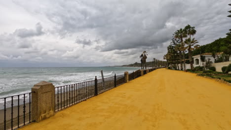 Toma-4k-De-Un-Amplio-Sendero-Junto-A-La-Playa-En-Un-Día-Nublado-Línea-Costera-En-Marbella,-Málaga,-España,-Costa-Del-Sol