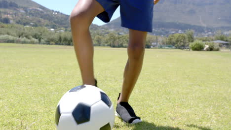 a person is about to kick a soccer ball on a sunny field with mountains in the background