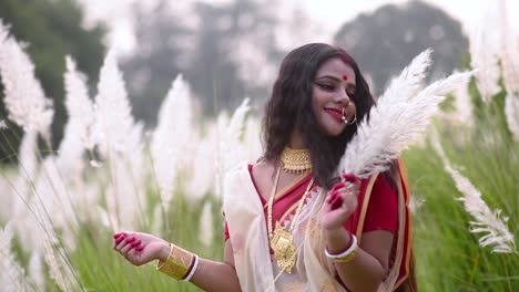 a married happy and elegant indian woman is playing with kaash phool white flowered grass on a windy day, sunset or sunrise