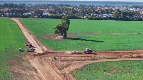 antena de un tractor y un escalador que pasa por delante de otros vehículos agrícolas a lo largo de un camino de tierra