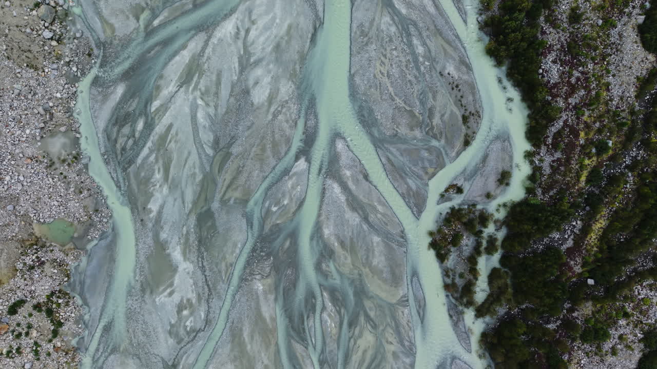 Drone pans downward in full top-down view along braided glacial river and rocky terrain