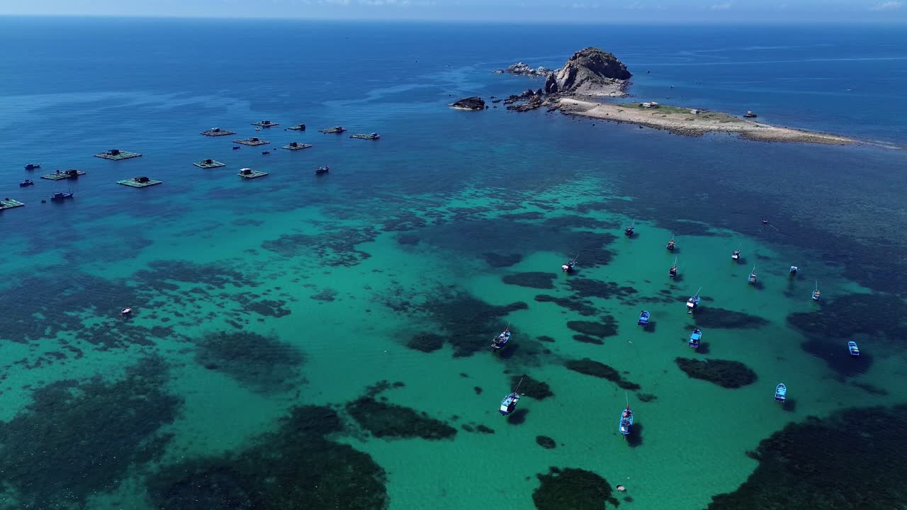 Semi orbit aerial shot of fishing boats near a rocky island, clear waters at Phan Rang in Ninh Hải District, Ninh Thuận, Vietnam