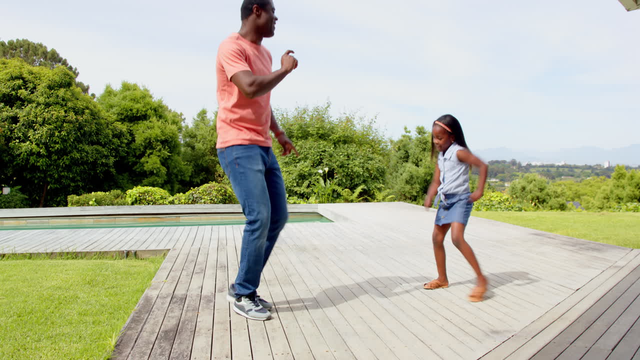 African American, Father and daughter dancing joyfully on wooden deck in sunny backyard