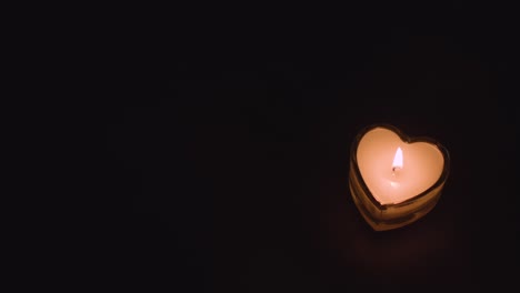 close up of romantic lit heart shaped white candles on black background with copy space