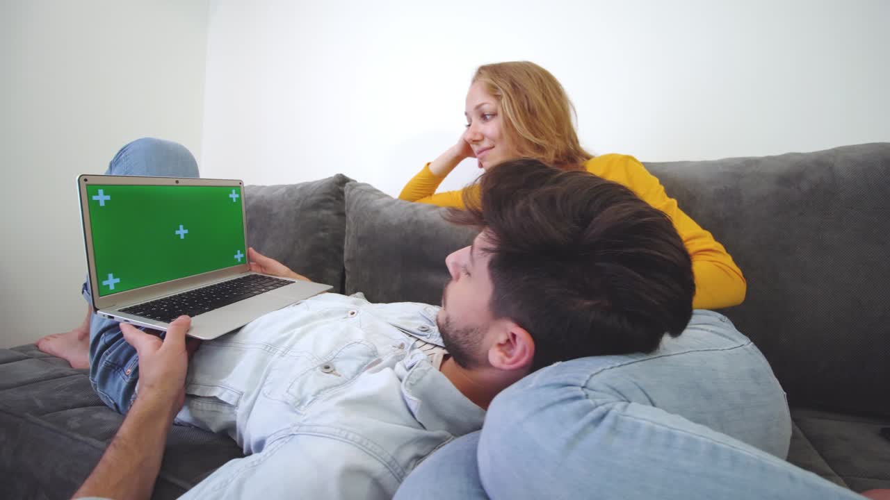 una pareja enamorada en un sofá mirando una computadora portátil. un niño tendido en el regazo de una niña. pantalla verde.