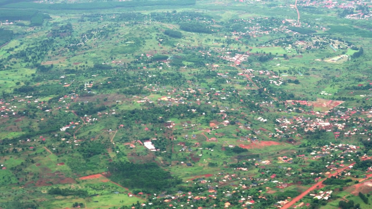 Naturskøn udsigt fra vinduesplads i et passagerfly, der flyver over Ugandas frodige grønne landskab, spredte huse og landlige landsbyer, filmet under en flyvning nær Entebbe.