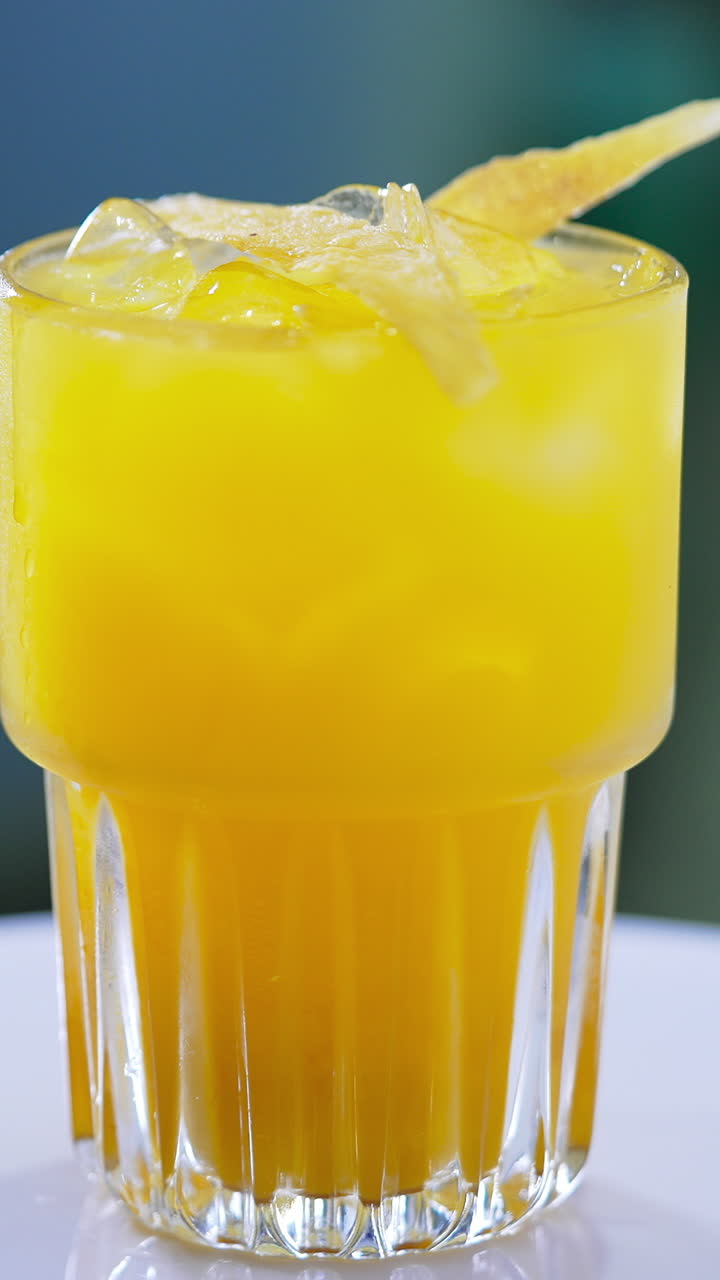 Orange tasty cocktail decorated with ice cubes and chips. Beautiful beverage on the spinning table close up. Vertical video
